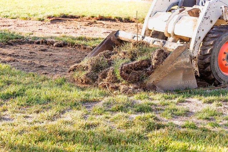 Small bulldozer removing grass from yard preparing for pool installation