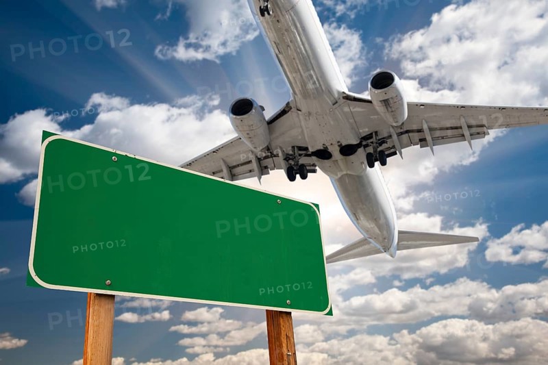 Blank green road sign and airplane above with dramatic blue sky and clouds