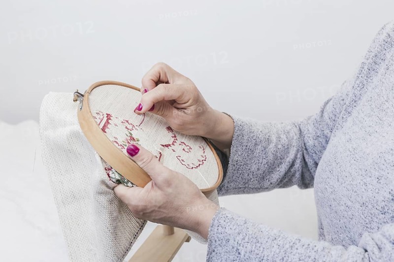 woman s hand cross stitching pattern on a hoop against white background