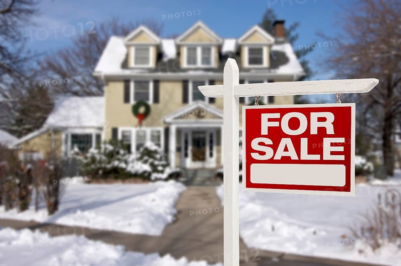 Home for sale real estate sign in front of beautiful new house in the snow