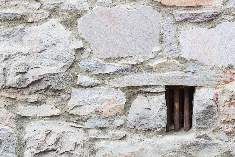 Old stone wall with small iron barred prison cell window