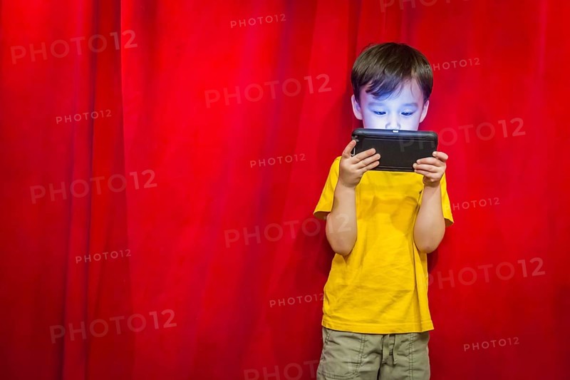 mixed-race boy watching his cell phone in front of red curtain