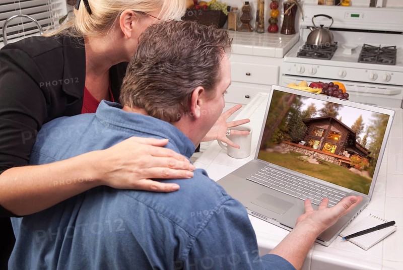 Couple in kitchen using laptop with lake cabin on the screen