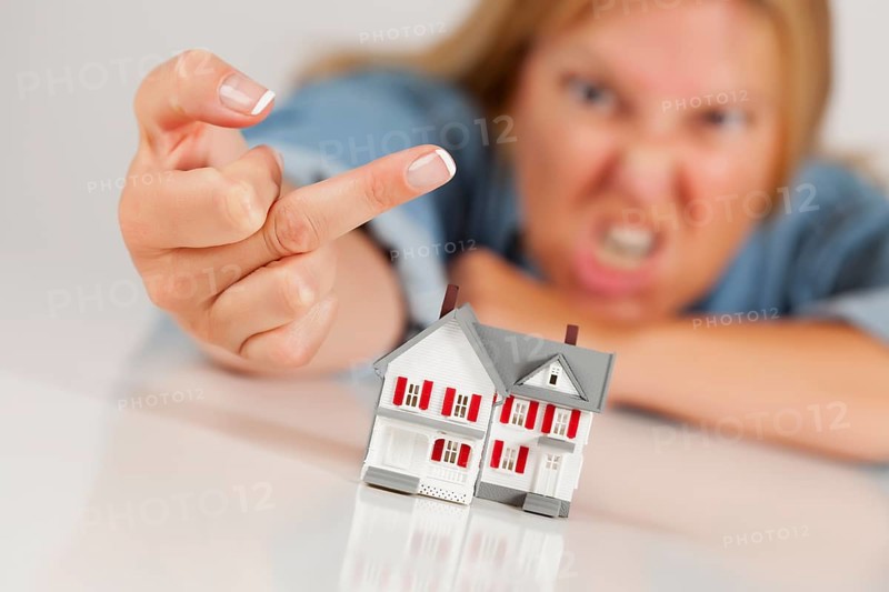 Angry woman flipping the bird behind model home on white surface