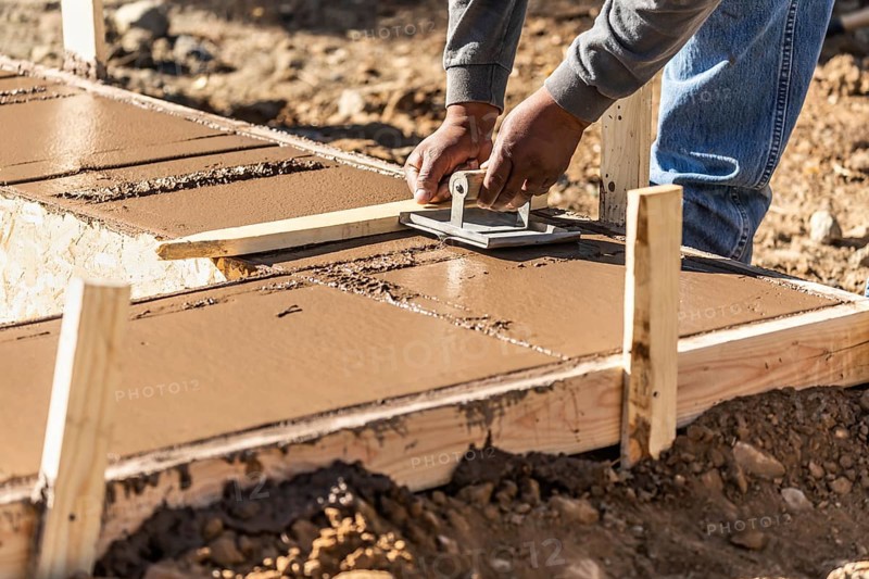 Construction worker using hand groover on wet cement forming coping around new pool