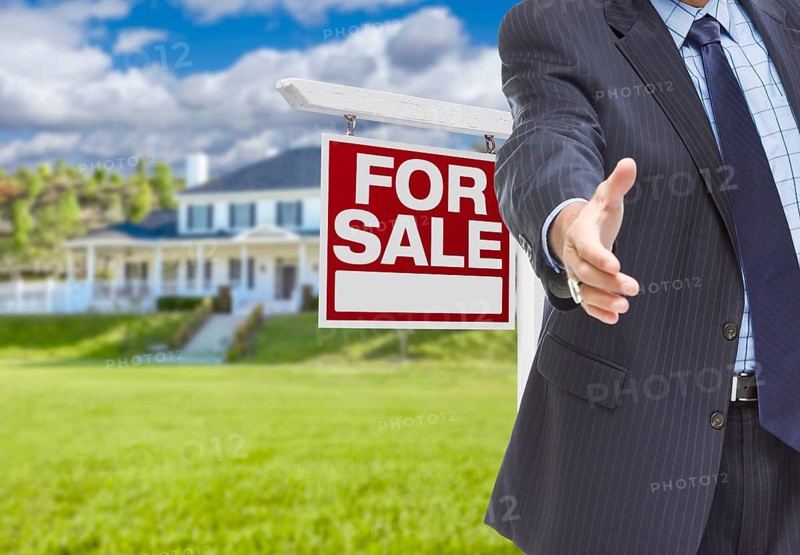 Real estate agent reaches for handshake with sale sign and new house behind