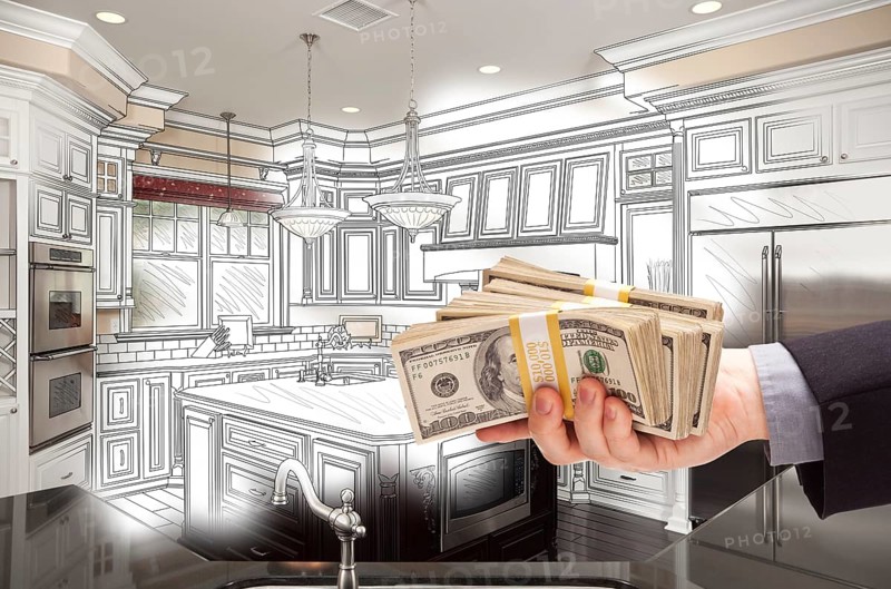Hand holding stacks of money over custom kitchen design drawing and photo combination