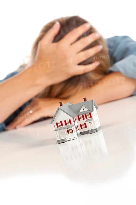 Woman with head in hand behind model home on a white surface