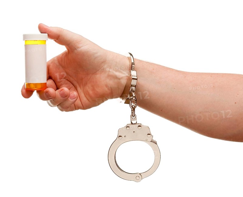 Handcuffed man holding blank medicine bottle isolated on a white background