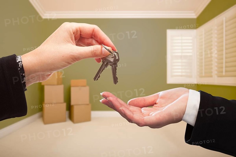 Woman handing over the house keys to A new home inside empty green colored room
