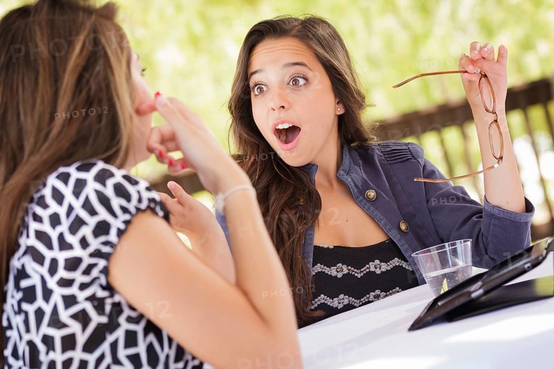 Expressive young adult girlfriends using their computer electronics outdoors