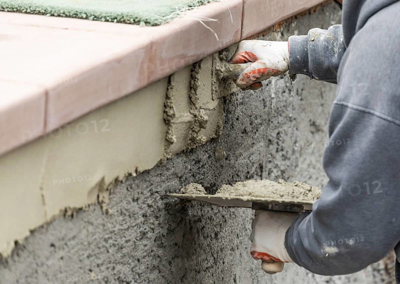 Tile worker applying cement with trowel at pool construction site