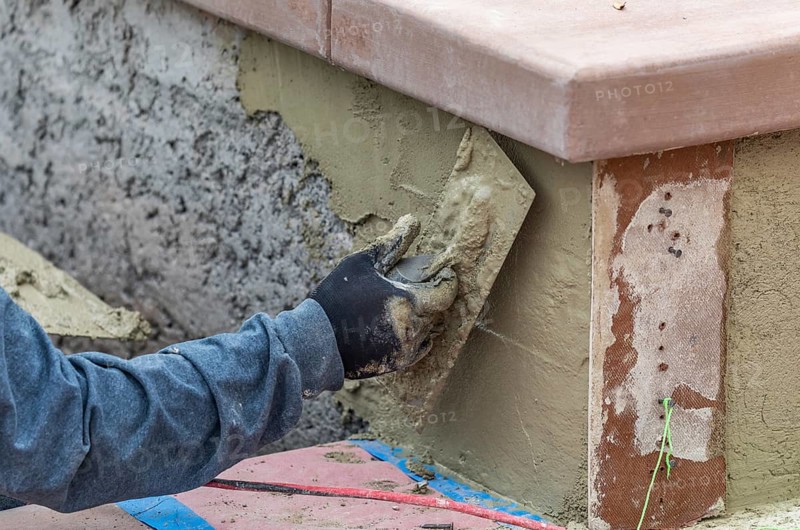Tile worker applying cement with trowel at pool construction site