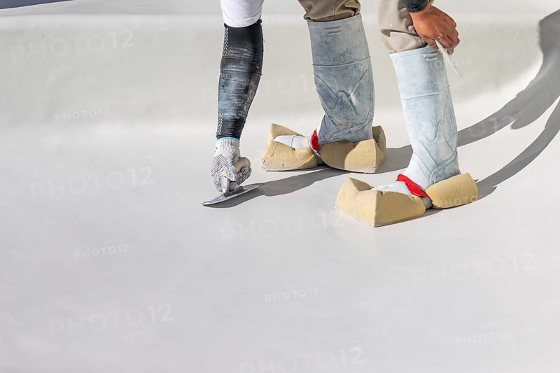 Worker wearing sponges on shoes smoothing wet pool plaster with trowel