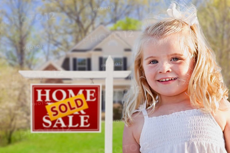 Cute smiling girl in front yard with sold for sale real estate sign and house