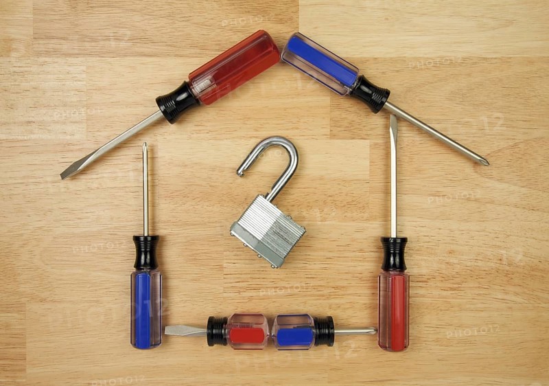 House shaped by screwdrivers and lock on a wood background
