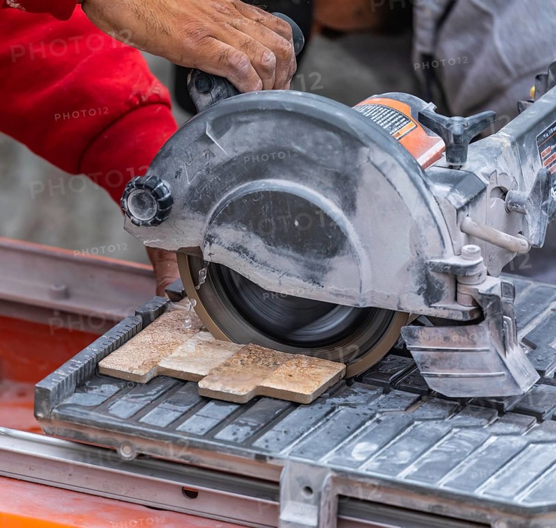 Worker using wet tile saw to cut wall tile at construction site