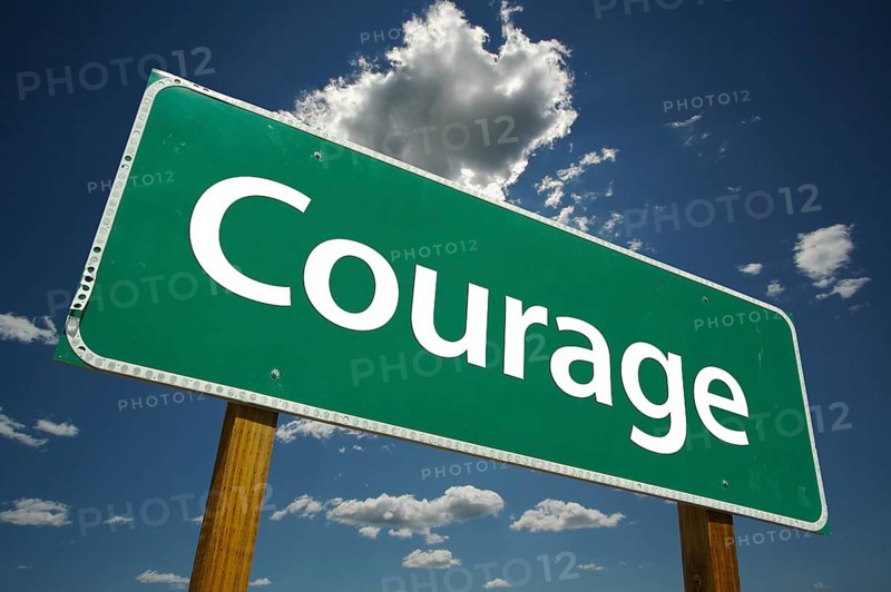 Courage green road sign over dramatic clouds and sky
