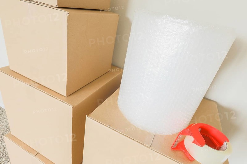 Variety of packed moving boxes with materials in empty room against wall