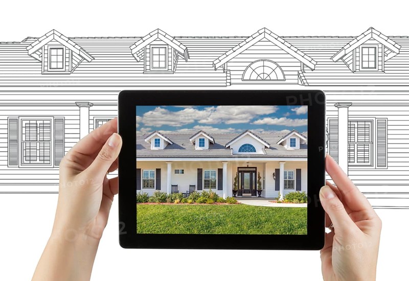 Female hands holding computer tablet with house photo on screen & drawing behind