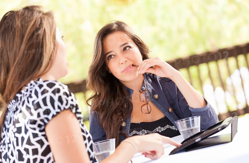 Expressive young adult girlfriends using their computer electronics outdoors