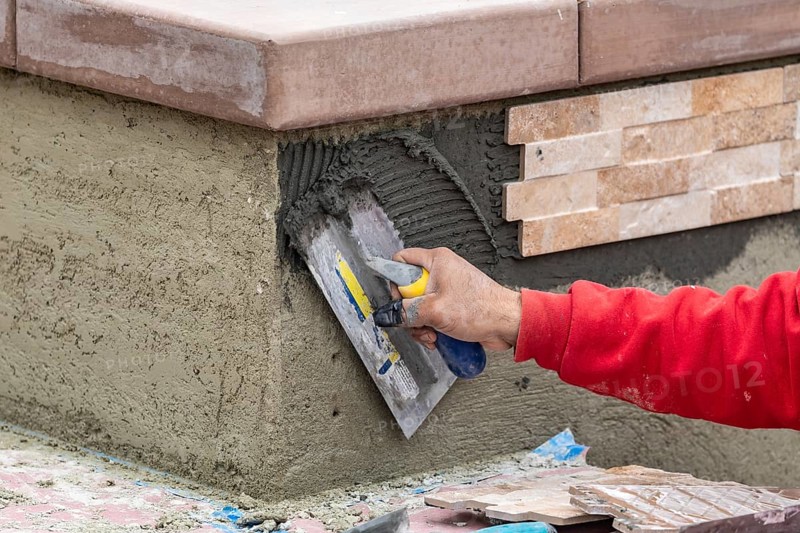 Worker installing wall tile cement with trowel and tile at construction site