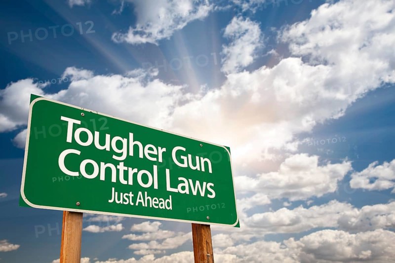 Tougher gun control laws green road sign with dramatic clouds and sky