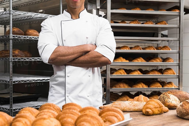 midsection male baker with his arms crossed standing bakery