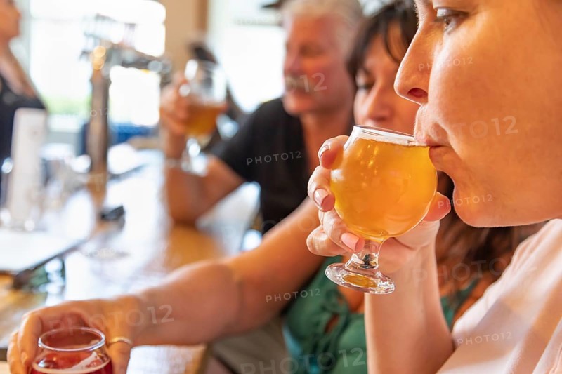 Female sipping glass of micro brew beer at bar with friends