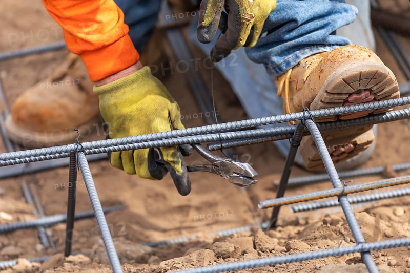 Worker securing steel rebar framing with wire plier cutter tool at construction site