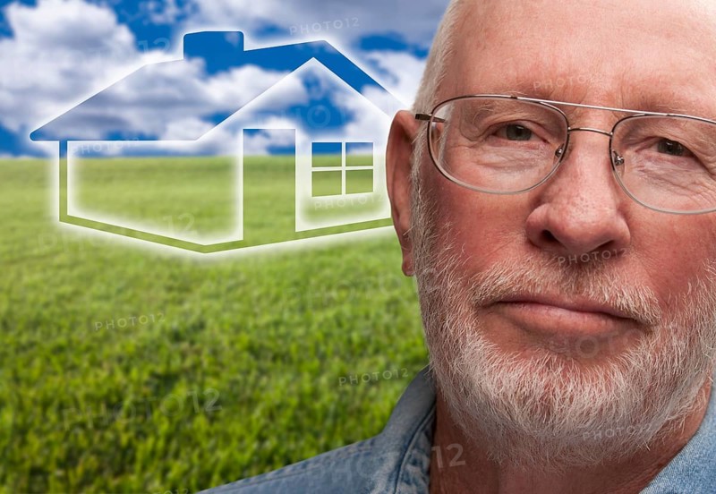 Melancholy senior man with green grass field and ghosted house behind him