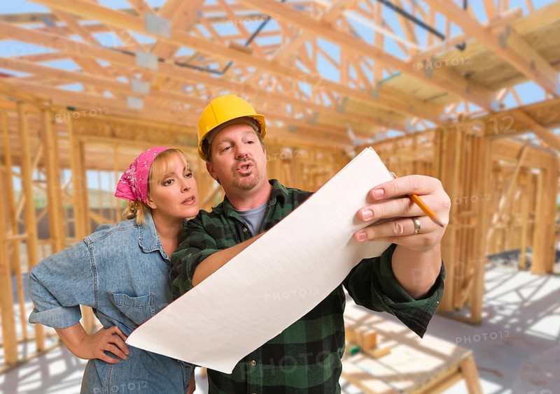 Contractor showing plans to woman on site inside new home construction framing