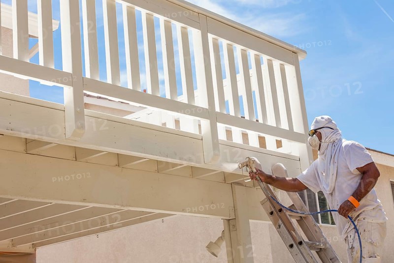 House painter wearing facial protection spray painting A deck of A home
