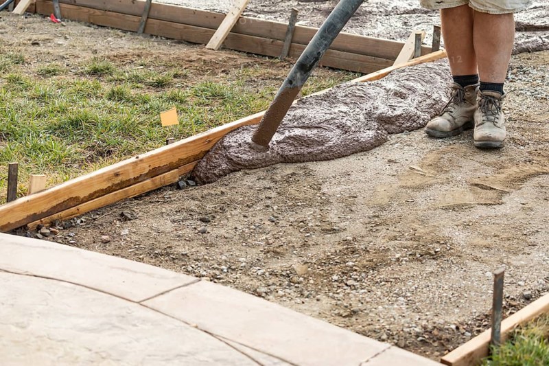 Construction worker pouring wet deck cement into wooden frame