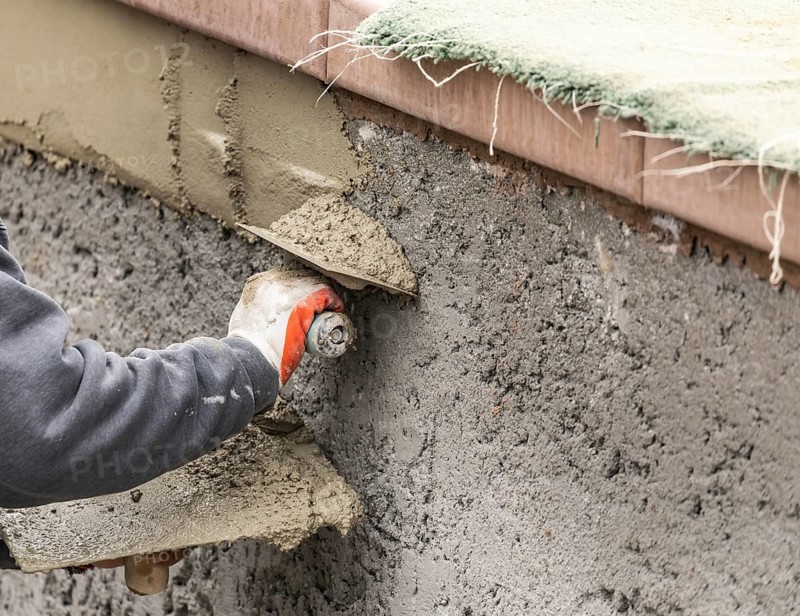 Tile worker applying cement with trowel at pool construction site