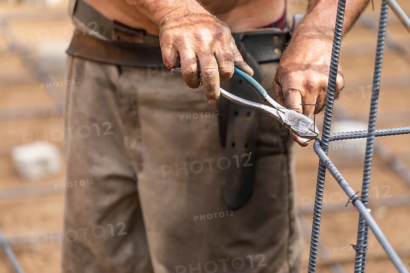 Worker securing steel rebar framing with wire plier cutter tool at construction site