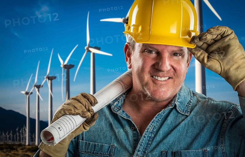 Smiling contractor in hard hat holding extention cord outdoors near wind turbines