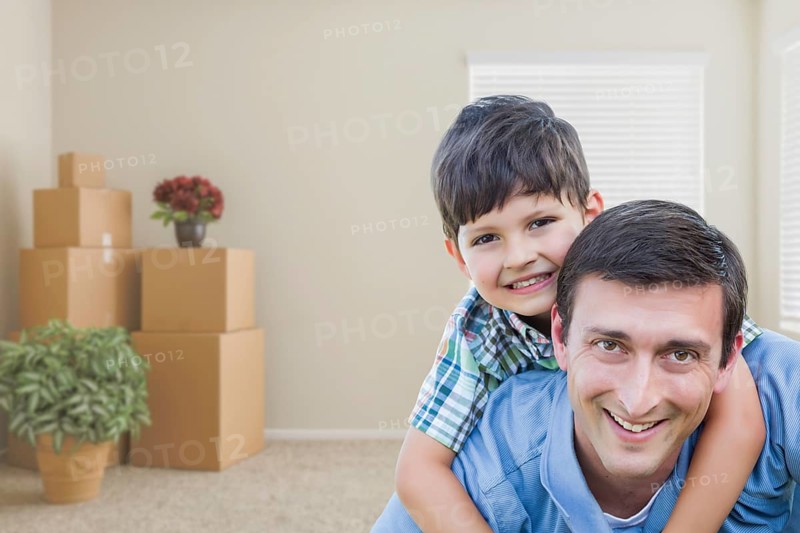 Happy father and son in room with packed moving boxes and potted plants