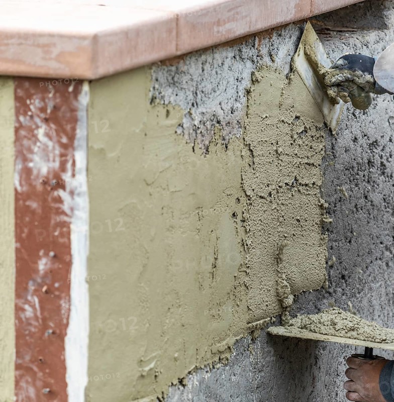 Tile worker applying cement with trowel at pool construction site