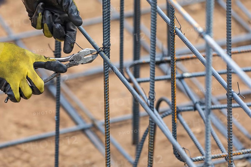 Worker securing steel rebar framing with wire plier cutter tool at construction site