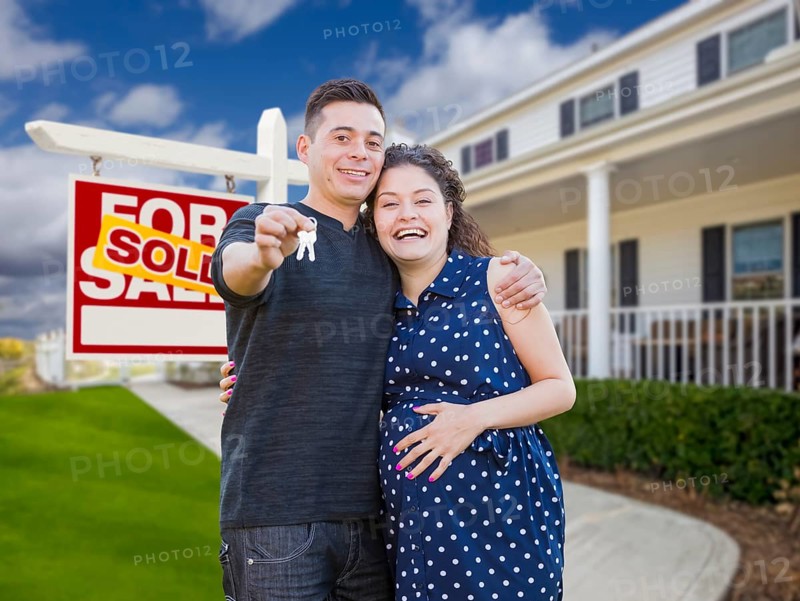 Happy hispanic couple in front of new home and sold real estate sign showing off their house keys