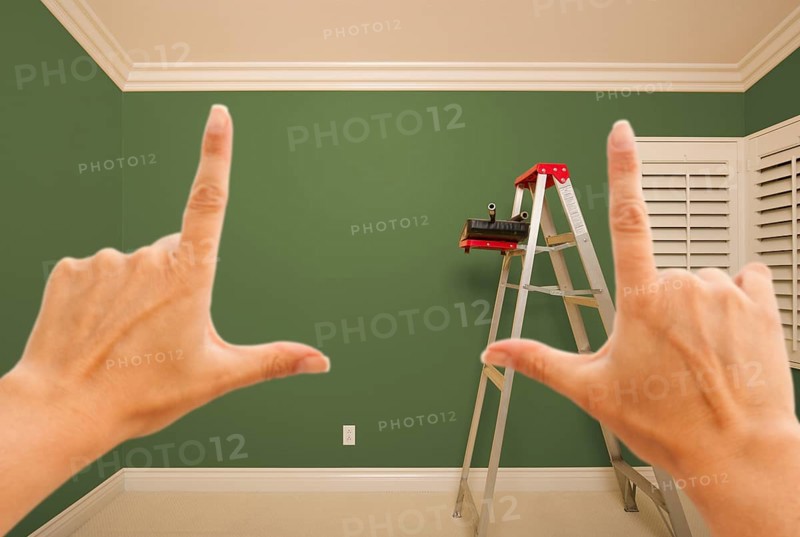 Hands framing green painted room wall interior with ladder