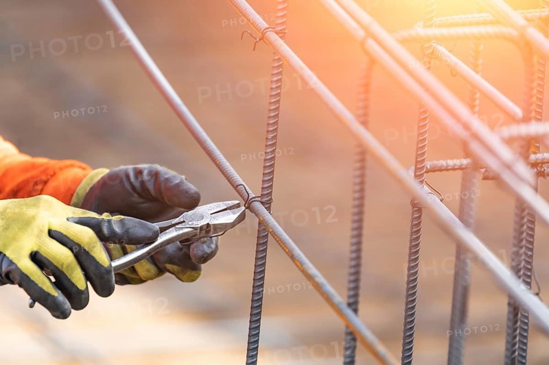 Worker securing steel rebar framing with wire plier cutter tool at construction site