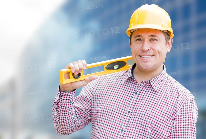 Young male contractor with hard hat and level in front of building