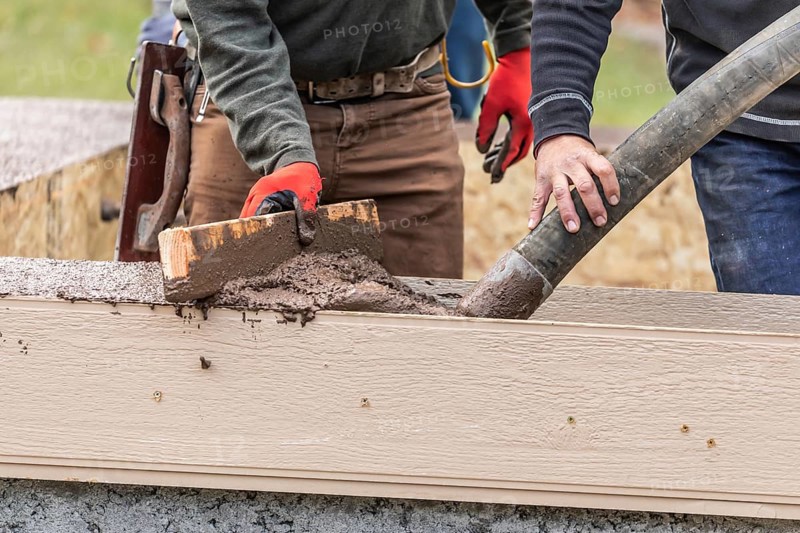 Construction workers pouring and leveling wet cement into wood framing