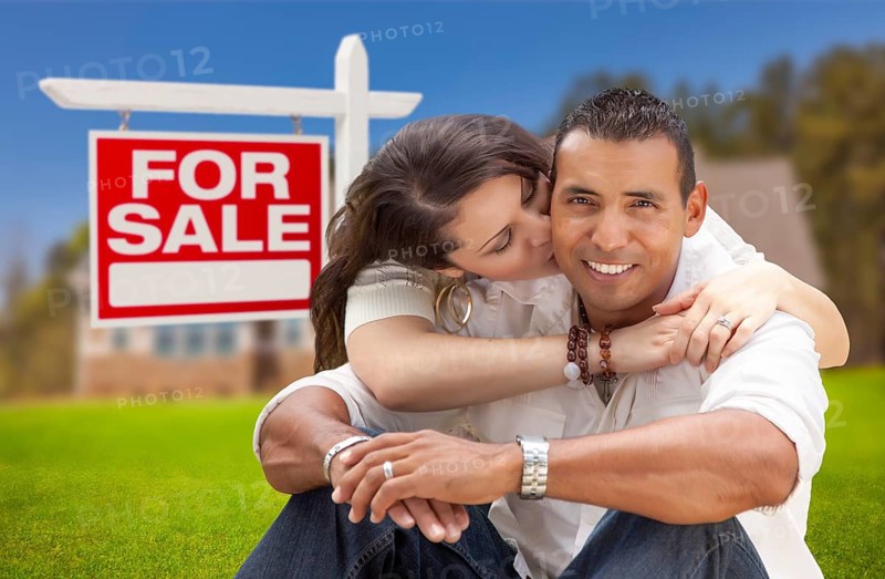 Young happy hispanic young couple in front of their new home and for sale real estate sign