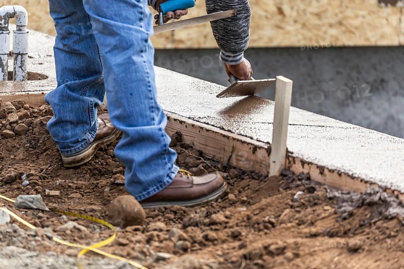 Construction worker using wood trowel on wet cement forming coping around new pool