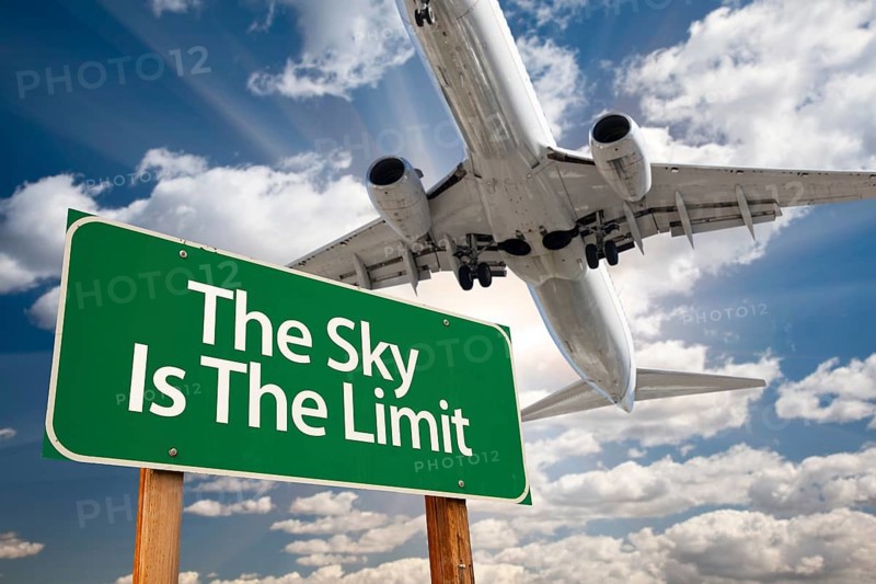 The sky is the limit green road sign and airplane above with dramatic blue sky and clouds