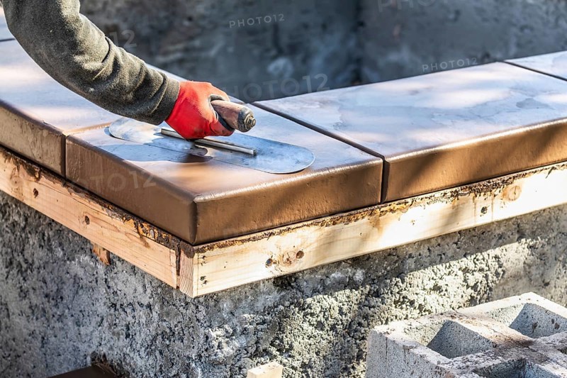 Construction worker using trowel on wet cement forming coping around new pool