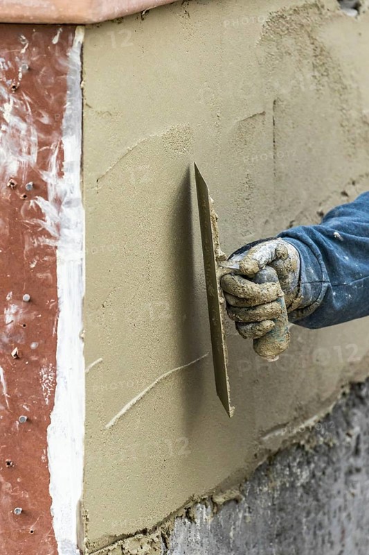 Tile worker applying cement with trowel at pool construction site